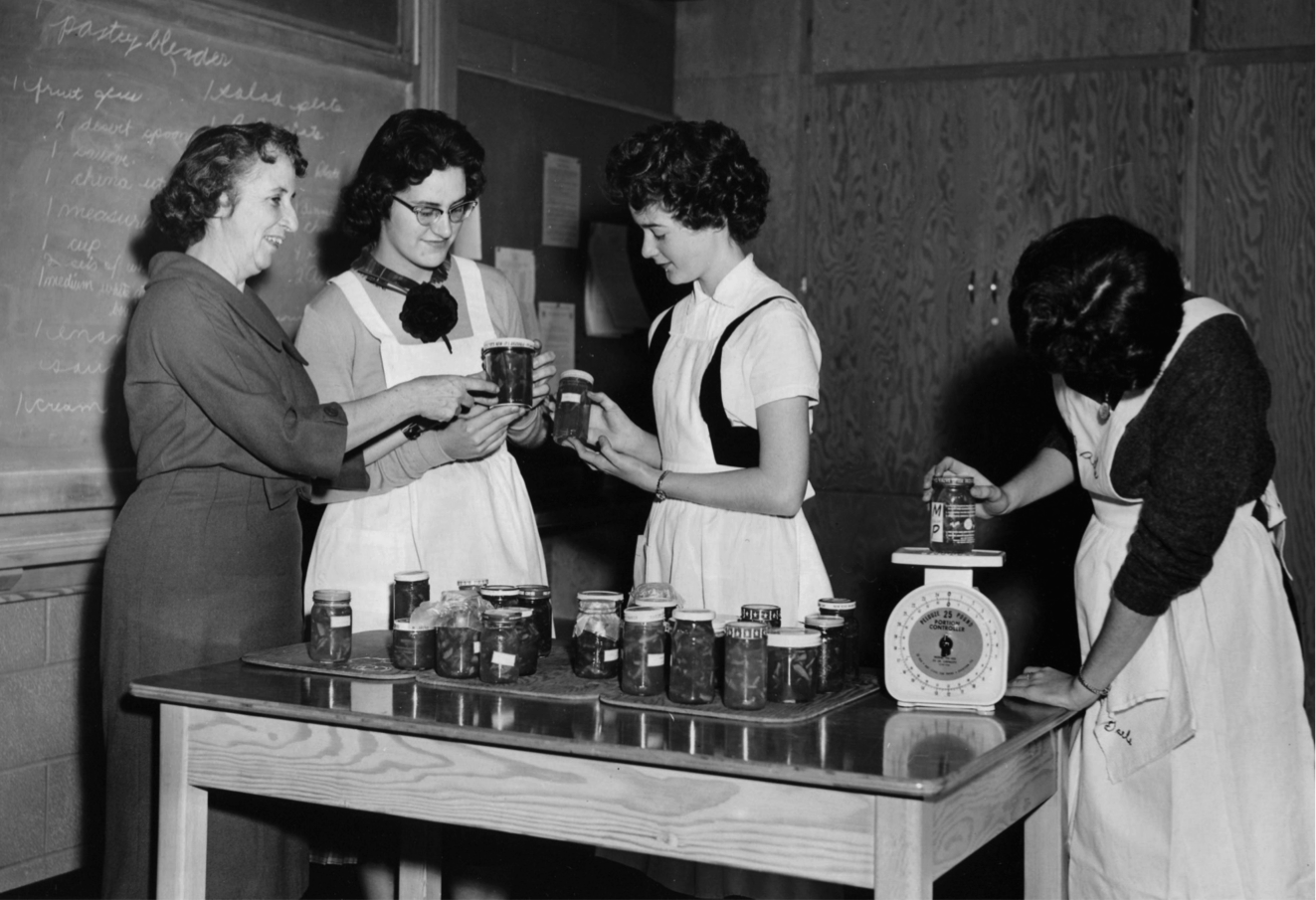 Miss Wilson and students in her Home Economics class examine bottles of marmalade (1960.)